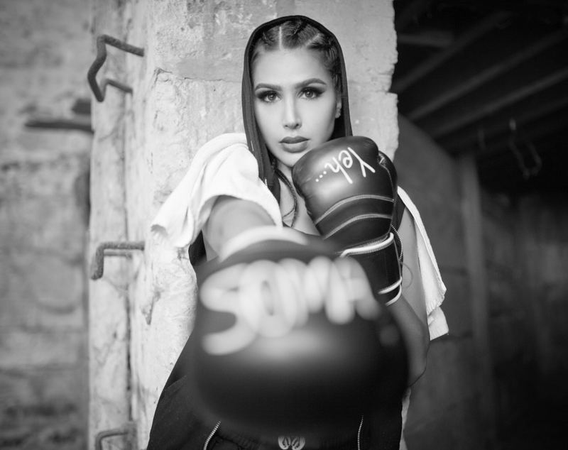 Somayeh en noir et blanc, capuche sur la tête et serviette sur les épaules, le poing ganté tendu vers l’objectif