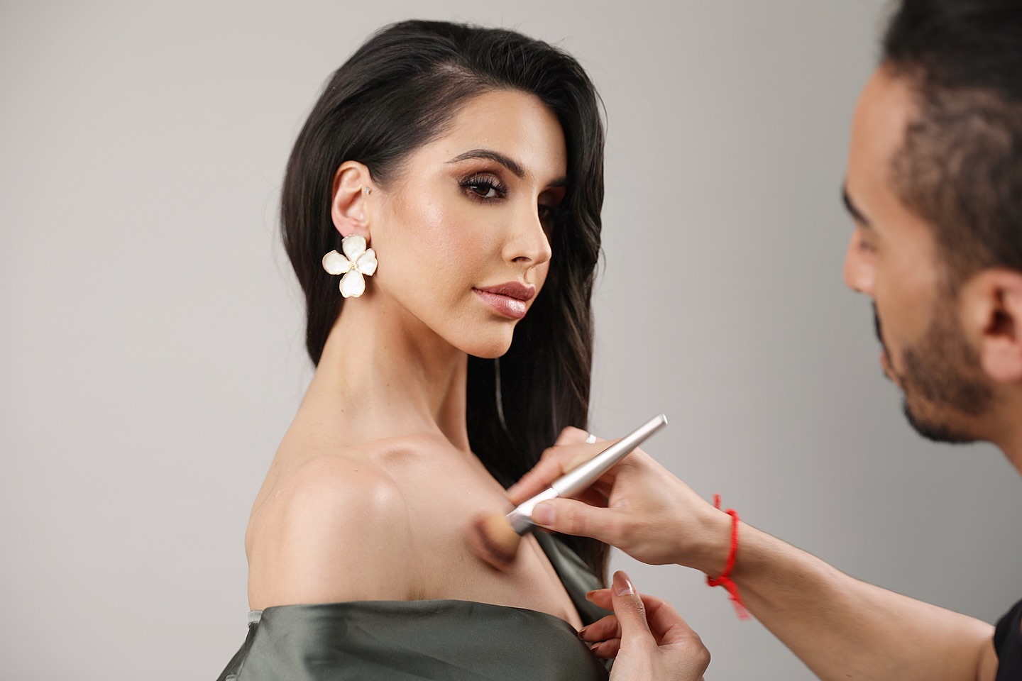 Somayeh pendant une séance de maquillage, boucle d’oreille fleur blanche, épaule nue et satin vert